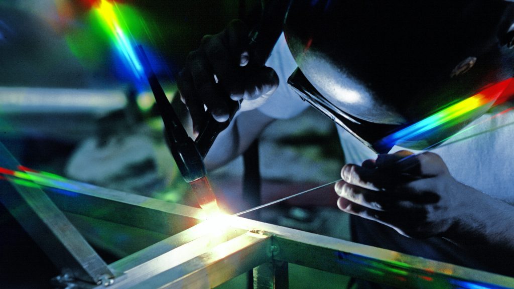 Westlake Environmental Fabrication - Person Welding with blinding arc causing prism effect, blue wash background